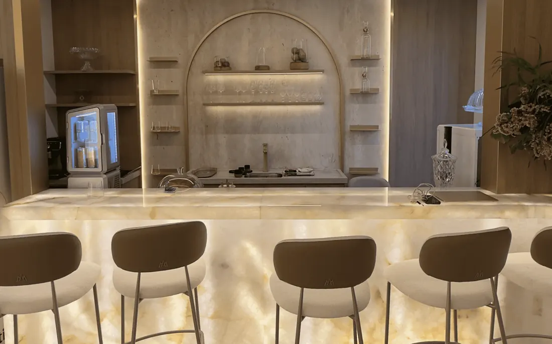 Copa do Instituto Evollution: bancada de ônix retroiluminada com banquetas altas, taças em prateleira e frigobar de bebidas